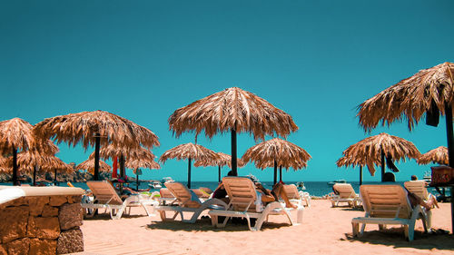 Palm beach umbrellas on beach against clear blue sky