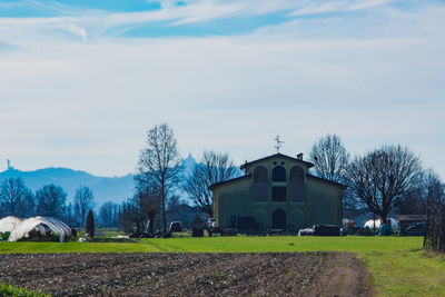 House on field by trees against sky