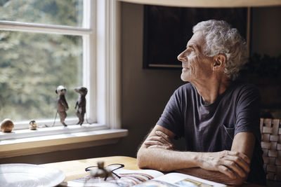 Contemplative senior man looking through window at home