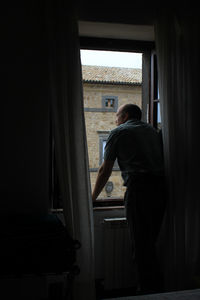 Rear view of man looking through window