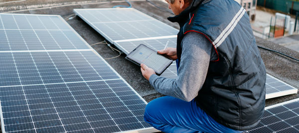 Man programming solar panel through digital tablet on roof