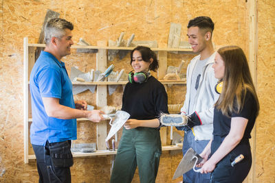 Confident carpenter holding equipment while standing with trainees at workshop during training