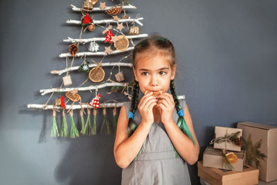 Smiling girl eating orange slice while looking away against christmas tree hanging on wall