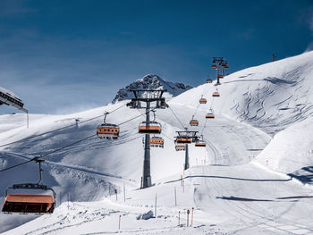 Ski lift by snow covered mountain against sky