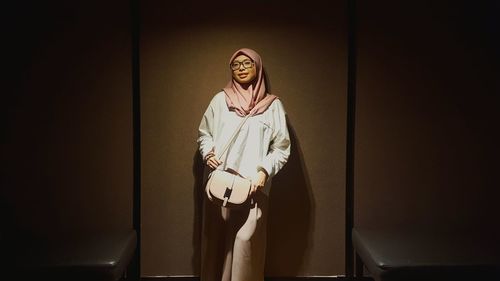 Portrait of young woman standing against wall at home