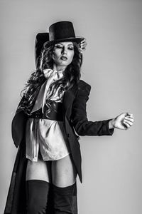 Portrait of young woman wearing hat standing against gray background