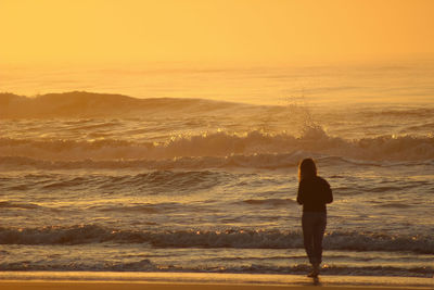 Rear view of woman standing on shore at beach during sunset