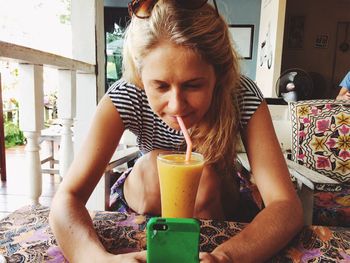 Woman drinking juice while using mobile phone at home