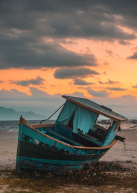 Boat moored on beach against sky during sunset