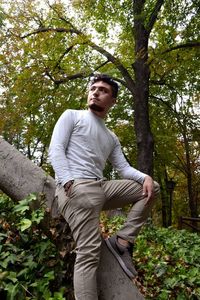 Young man standing by tree in forest
