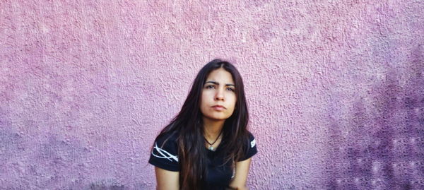 Portrait of a beautiful young woman standing against pink wall