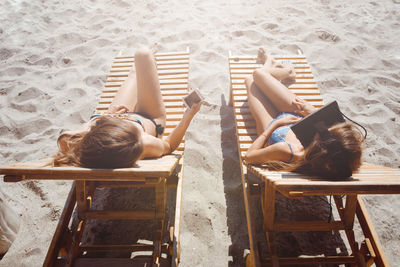 Female friends sitting on lounge chairs at beach