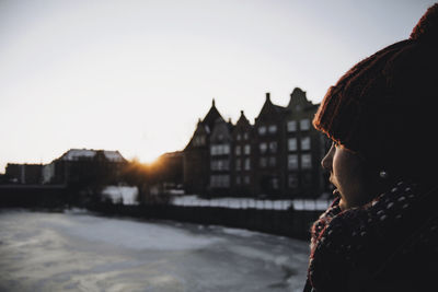 Woman against river and buildings in city during sunset