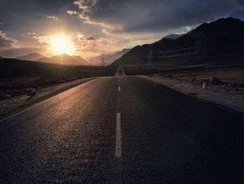 Road leading towards mountains against sky during sunset