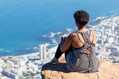 Rear view of woman sitting on rock by sea