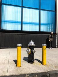 Full length of man standing against building with fire hydrants at sidewalk