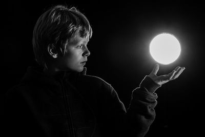 Optical illusion of boy levitating illuminated glowing sphere against black background