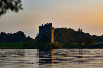 View of building by lake against sky during sunset