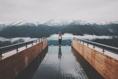 Rear view of woman standing on snowcapped mountain against sky