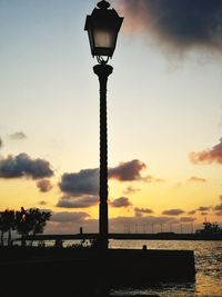 Silhouette street light by sea against sky during sunset