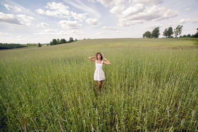 Young woman with long black hair stands in white dress and clothes straw hat is on the green field 