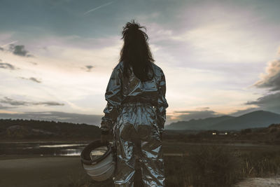 Woman astronaut holding space helmet at beach