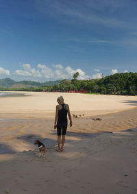 Rear view of woman with dog standing at beach against sky