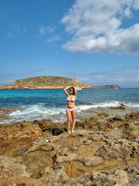 Full length of shirtless man standing on rock at beach against sky