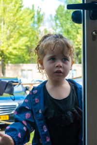Little girl stands outside the house seen through the glass door