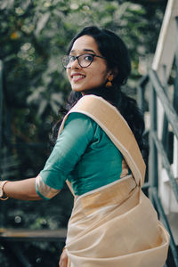 Portrait of a young woman standing against tall trees taken during the onam festival 