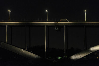 Illuminated street lights by bridge against sky at night