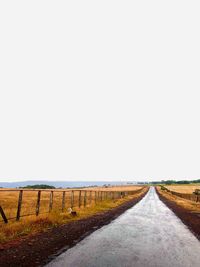Empty road amidst field against clear sky