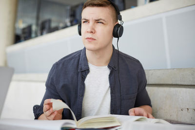 Young student with headphones turning pages while studying at table in university