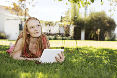Grl with long red hair lying in grass with tablet