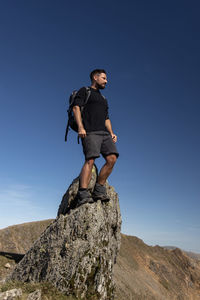 Low angle view of young man on rock against clear blue sky