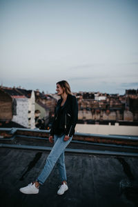 Full length of happy young woman standing on building terrace against sky in city