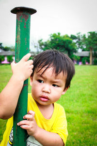 Portrait of cute boy looking away while holding pole outdoors