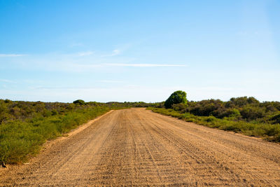 Dirt road amidst field against sky