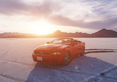 Vintage car on sea shore against sky during sunset