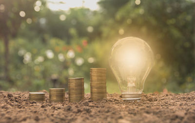 Close-up of illuminated light bulb with stacked coins on field