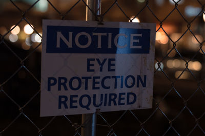 Close-up of chainlink fence with information sign at night