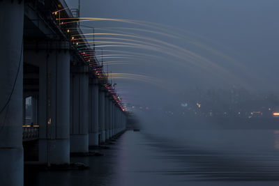 Low angle view of water flowing from bridge in river against sky at dusk