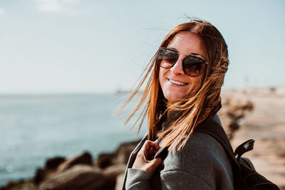 Side view portrait of happy woman with tousled hair standing on pier over sea against clear sky