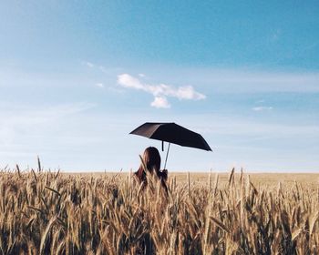 Rear view of woman holding umbrella while standing amidst crops