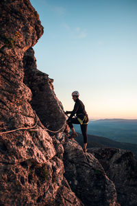 Concept: adventure. climber woman with helmet and harness. silhouette at sunset on the mountain. profile. resting looking at the climbing route. via ferrata in the mountains.