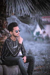 Young man looking away while sitting outdoors