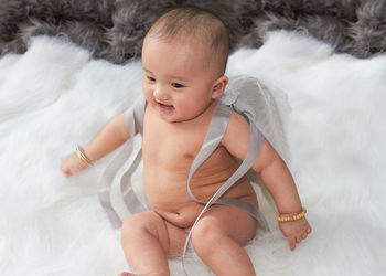 High angle view of cute baby girl sitting over fur blanket on bed at home