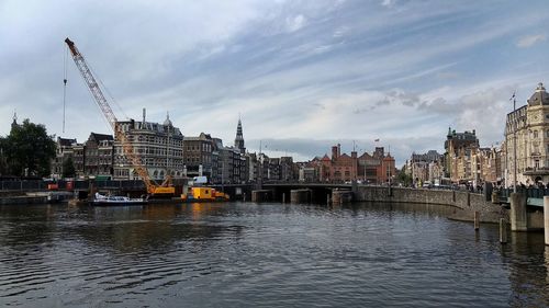 Bridge over river by buildings in city against sky