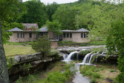 Stream flowing to waterfall amidst trees and house in forest