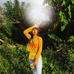 Woman shielding eyes while standing against plants in park